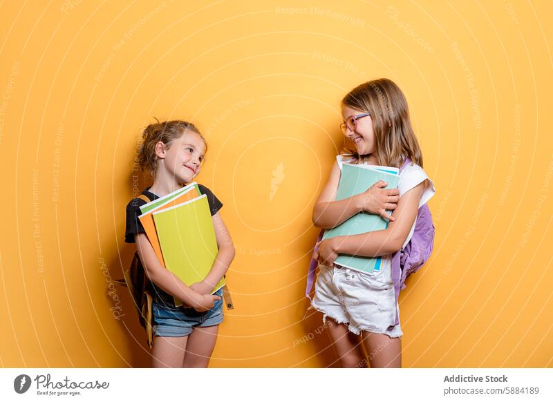 Schulmädchen mit lächelnden Büchern in einer Atelierumgebung Mädchen Schule Buch Lächeln Schüler gelb Hintergrund Rucksack Brille Bildung Glück heiter