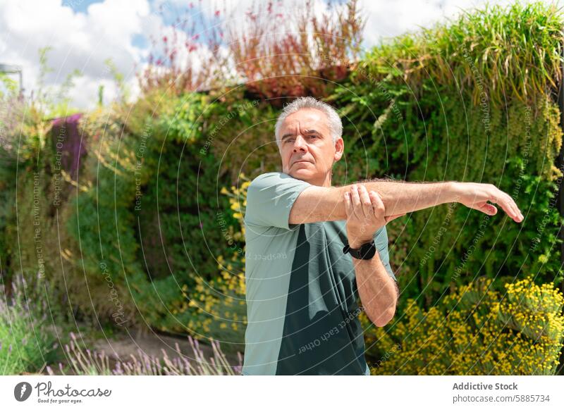 Älterer Mann streckt sich in einem üppigen grünen Park Senior strecken T-Shirt Übung Fitness Wohlbefinden reif Arme Vorbereitung pulsierend Laubwerk Garten