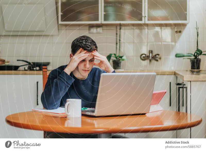 Junger Mann gestresst während einer Hausaufgabenstunde Stress Laptop heimwärts Küche Tisch lernen Arbeit müde unter Druck gesetzt Fokus Angst Bildung abgelegen