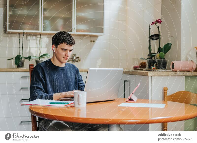 Junger Mann arbeitet von zu Hause aus in einer gemütlichen Küchenumgebung arbeiten heimwärts Laptop Tisch Kaffee Becher Pflanze sonnig Fokus