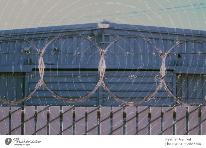Stacheldraht auf einem Zaun vor einem kleinen Industriegebäude abgezäunt Rasierdraht Garage Lagerhalle Industrielandschaft