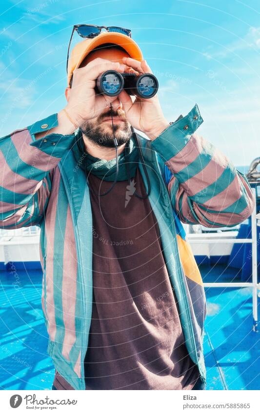 Mann beobachtet etwas durch ein Fernglas suchen erstaunt neugierig beobachten Mensch Hipster Blick entdecken Porträt bärtig modern blau grün Cap Schirmmütze