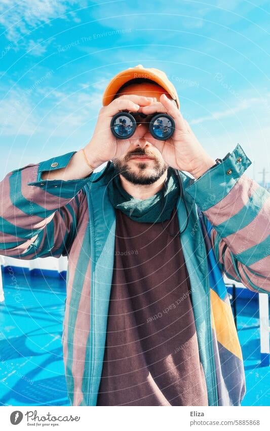 Mann, der etwas durch ein Fernglas beobachtet Suche erstaunt inquisitorisch beobachten Mensch Hipster Blick entdecken Porträt bärtig modern blau grün