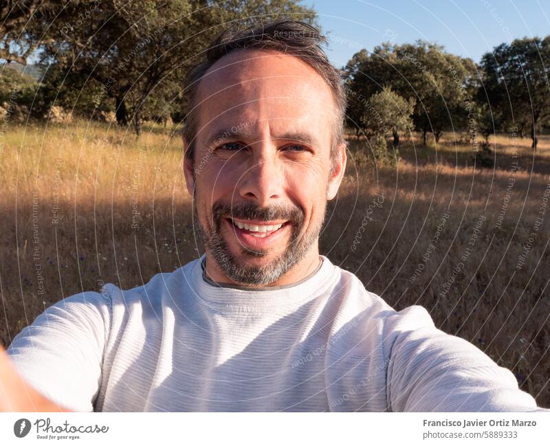 Mann nimmt Selfie in sonniger Landschaft auf dem Land Lächeln Glück Natur Feld im Freien Bäume Himmel Porträt Fotografie reisen Freizeit lässig Sommer malerisch