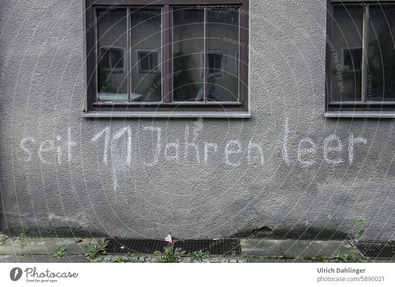 graue Hauswand mit Spruch in weißer Schrift : seit 11 Jahren leer Graffiti Immobilienkrise Wohnungsnot Fassade Immobilienmarkt Wohnungssuche Wohnen Miete haus
