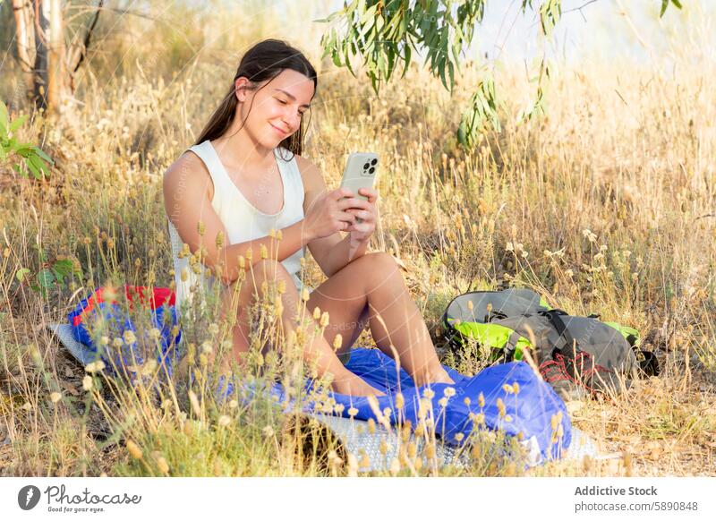 Junge Frau, die sich beim Wandern entspannt und ihr Smartphone benutzt jung wandern Pause Gras sitzend Rucksack Schatten Stilrichtung Lifestyle Natur im Freien