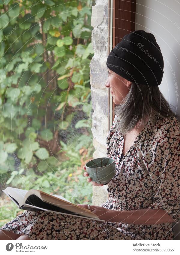 Frau genießt Tee und Buch am Fenster im Herbst lesen geblümt Kleid Baskenmütze im Innenbereich Gelassenheit friedlich Windstille Freizeit Erholung Laubwerk Grün