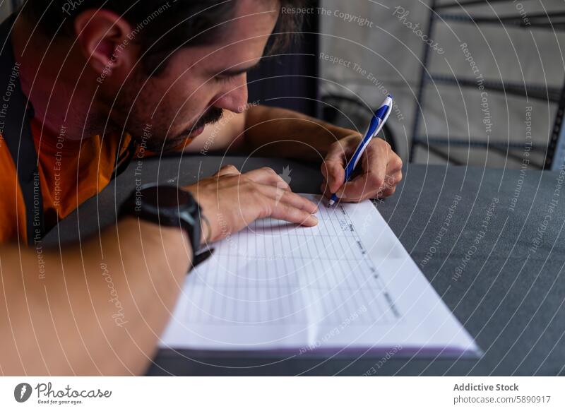 Ein Mann füllt in einem schwach beleuchteten Raum akribisch ein Arbeitsblatt aus Schriftstück Schreibstift Tisch Konzentration Detailaufnahme Büro lässig Hemd