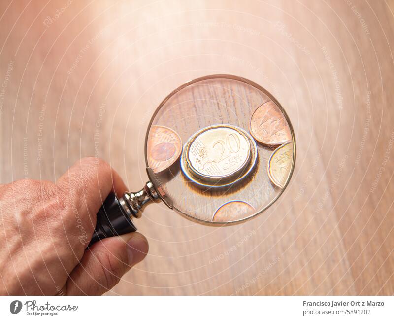 Hand hält Lupe über Münzen vergrößernd Glas Geldmünzen Nahaufnahme Detailaufnahme Prüfung Besichtigung Numismatik Währung Finanzen Sammlung Hobby Metall lernen