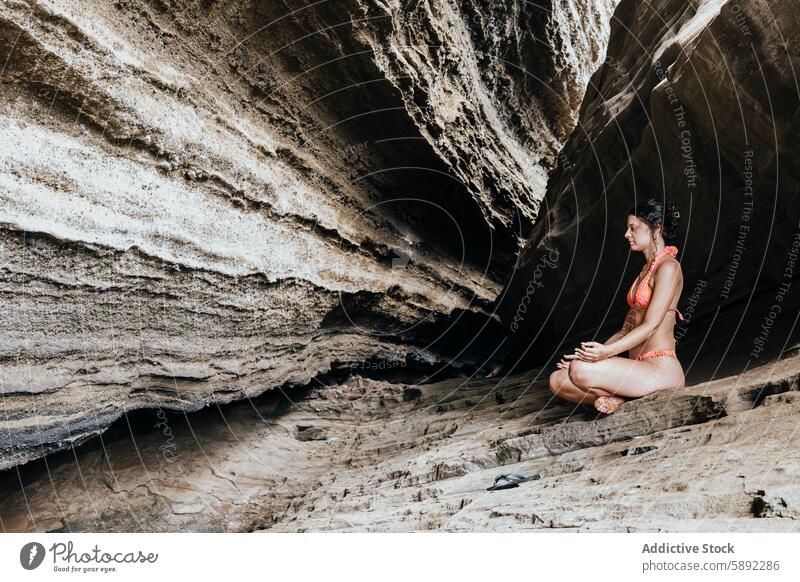 Frau meditiert in einer ruhigen Felsenhöhle im Sommerurlaub Meditation Feiertag Ruhe Höhle felsig Rückzug Gelassenheit Bikini rot jung friedlich abgelegen Natur