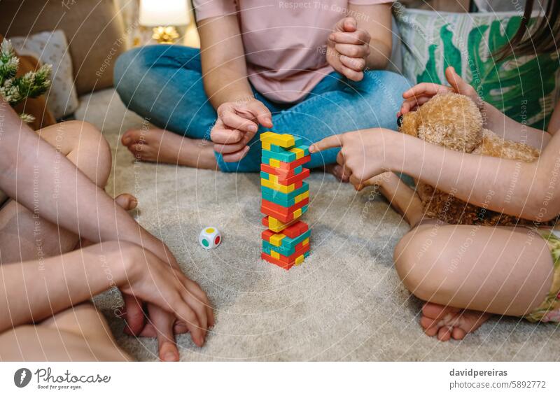 Unerkennbare Familie, die sich zu Hause auf dem Teppich mit einem Stapelspiel aus Holz vergnügt unkenntlich habend Spaß Spielen Zusammensein Kinder Spielfigur