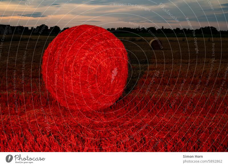 Strohballen in roter Beleuchtung vor einem ruhigen Abendhimmel und dörflicher Silhouette Rotlicht Ernte Landwirtschaft Dorfromantik Lichtstimmung