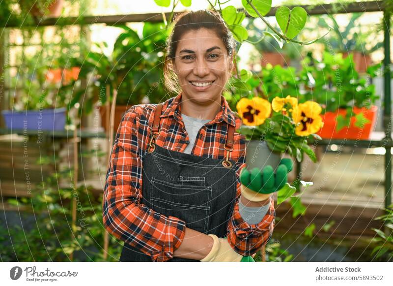 Glückliche Frau mit Blume in der Hand Gewächshaus eingetopft Lächeln positiv Pflanze Botanik Flora Gärtner Viola tricolor Gartenbau Wachstum heiter geblümt