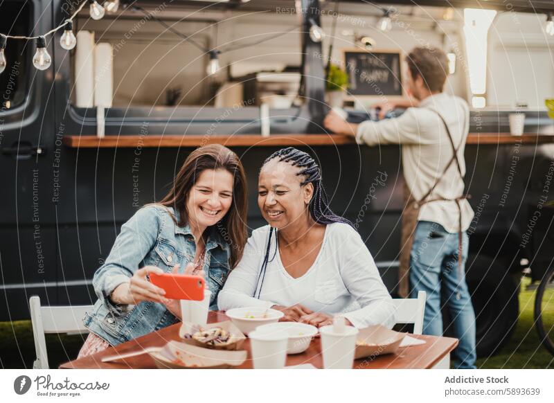 Erwachsene Frauen machen ein Selfie am Tisch in der Nähe des Food Trucks Lebensmittel Lastwagen Smartphone Lächeln Freund sitzen Kellner Glück Freundin