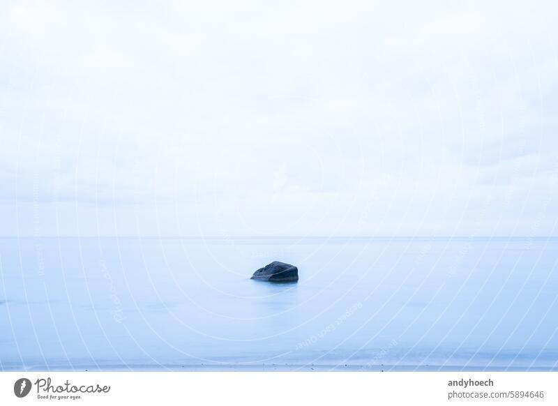 Ein einsamer Felsen im Meer in einem sanften Blau Strand Schönheit blau Unschärfe Felsbrocken Windstille wolkig Küste Küstenlinie dramatisch träumen Leere leer