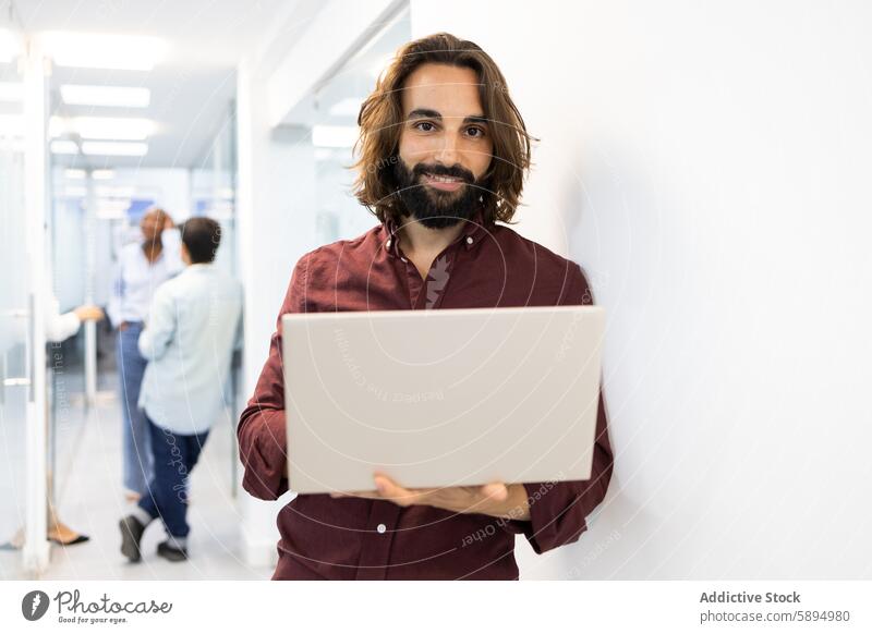 Engagierter Pädagoge mit Laptop in einem belebten Korridor der Akademie Gang Kollege Interaktion Lächeln Vollbart männlich Erwachsener professionell Bildung