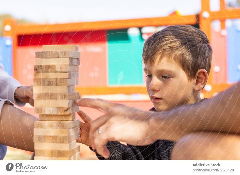 Junge spielt mit seiner Familie auf dem Spielplatz Klotz Stapel Jenga Strategie Mutter Sohn spielen Konzentration Herbst im Freien Freizeit Fokus Anschluss