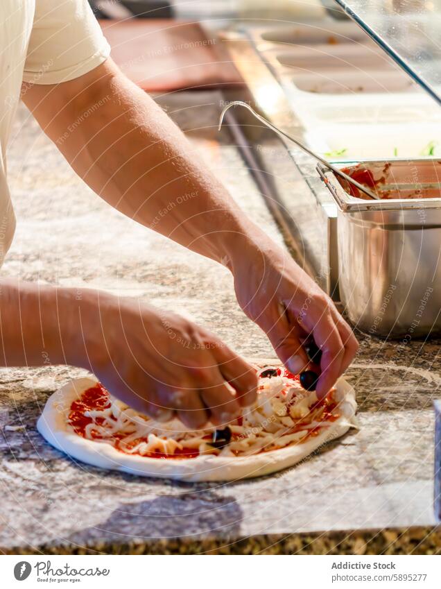 Hände, die in der Küche eine Pizza mit frischem Belag zubereiten Vorbereitung Hand Käse Saucen oliv Lebensmittel Essen zubereiten Bestandteil backen Teigwaren