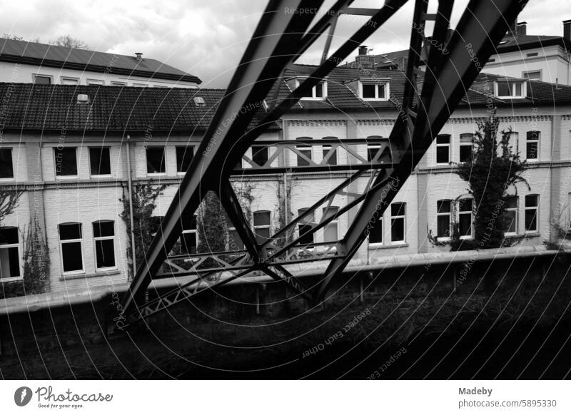 Stahlträger der Wuppertaler Schwebebahn und Häuserzeile mit restaurierten Altbauten bei Regenwetter in Wuppertal im Bergischen Land in Nordrhein-Westfalen in neorealistischem Schwarzweiß