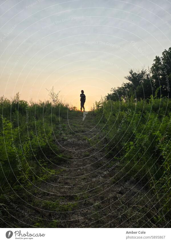 Männlicher Teenager auf dem Gipfel eines grasbewachsenen Hügels bei Sonnenuntergang Sonnenuntergangshimmel grasbewachsener Hügel männlicher Teenager