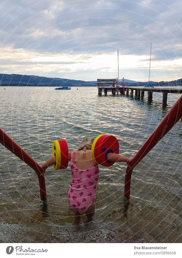 Kleines Mädchen in rosa Badeanzug mit Schwimmflügeln steigt in den See Attersee baden Schwimmen & Baden schwimmen Steg Gegenlicht Gegenlichtaufnahme