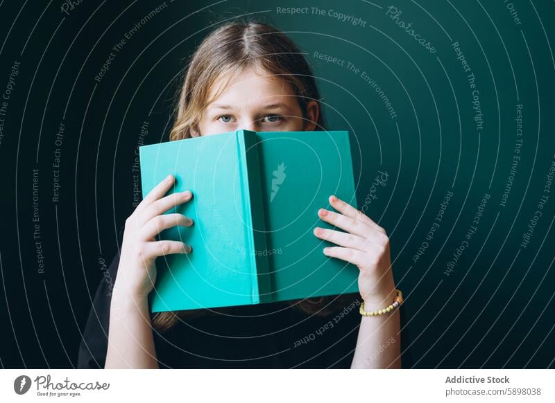 Junges Mädchen, das über ein grünes Buch hinweg in die Kamera blickt Schüler Bildung in die Kamera schauen zurück zur Schule lernen Lernen Leser Jugend
