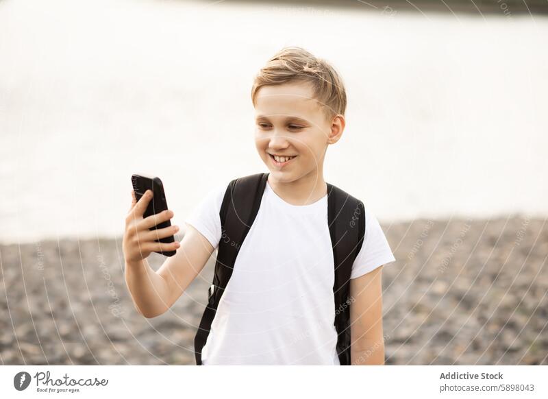 Teenager Junge nimmt Selfie mit Smartphone im Park in der Nähe eines Teiches Handy im Freien Glück Lächeln Blick auf den Bildschirm See Video vlog Blogger