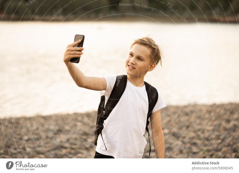 Teenager, der ein Selfie mit einem Smartphone in einem Park in der Nähe eines Sees macht Junge Handy im Freien Video vlog Blogger Reisender Glück Aufnahme