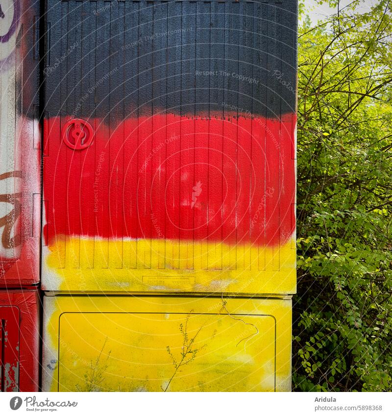 Schwarz, Rot, Gelb besprühter Stromkasten mit Hecke Deutschland schwarz-rot-gold Farbe Graffiti Deutsche Flagge Nationalflagge Deutschlandfahne Politik & Staat