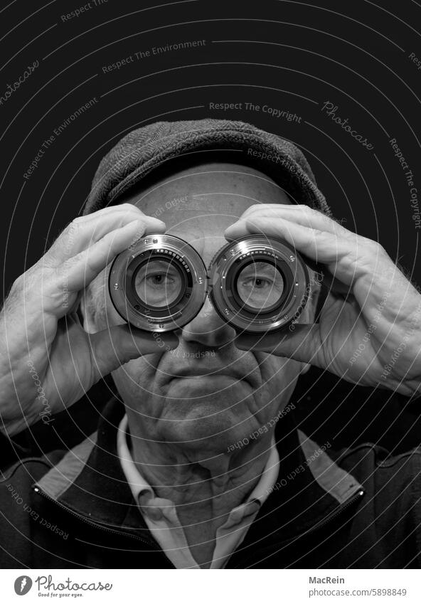 Mann schaut durch zwei Objektive mann objektiv objektive mütze guckt durchblick optik brille halten