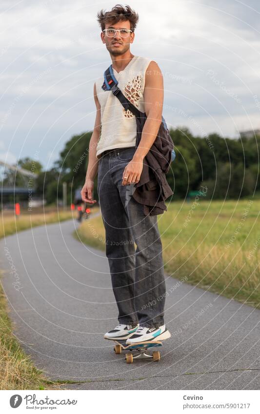 Junger Mann aus Indien fährt Skateboard Sportlich Sexy Muskulös Freundlich Sympathisch Blick in die Kamera lustvoll Außenaufnahme Natur grün erotisch Bart Fluss