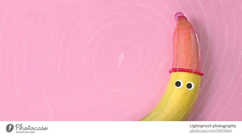 Banane mit Glotzaugen und rotem Kondomhut auf rosa Hintergrund. Safe Sex Konzept. Kulleraugen Anthropomorphe Humor Sexualerziehung ein Gesicht machen Auge