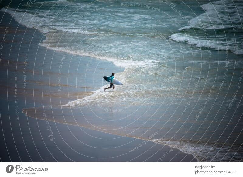 Ein Shortboard Sportler geht vom Strand auf das wellige Meer um zu Surfen. Blick von der Seite Wellen Surfbrett Wasser Wassersport Mann Lifestyle sportlich