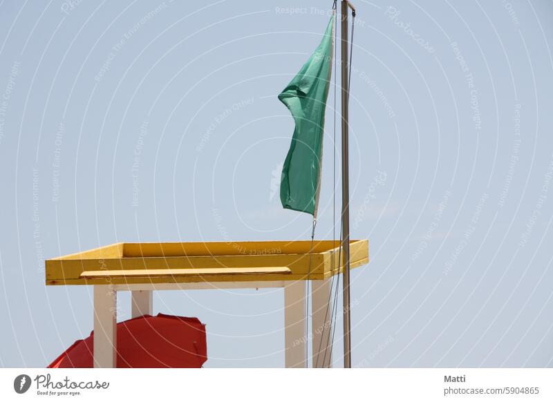 Grüne Flagge am Rettungsschwimmer-Hochsitz mit rotem Sonnenschirm grün Fahne Rettungschwimmer Lifeguard Strand Schwimmen Meer schwimmen erlaubt Himmel Wind Sand