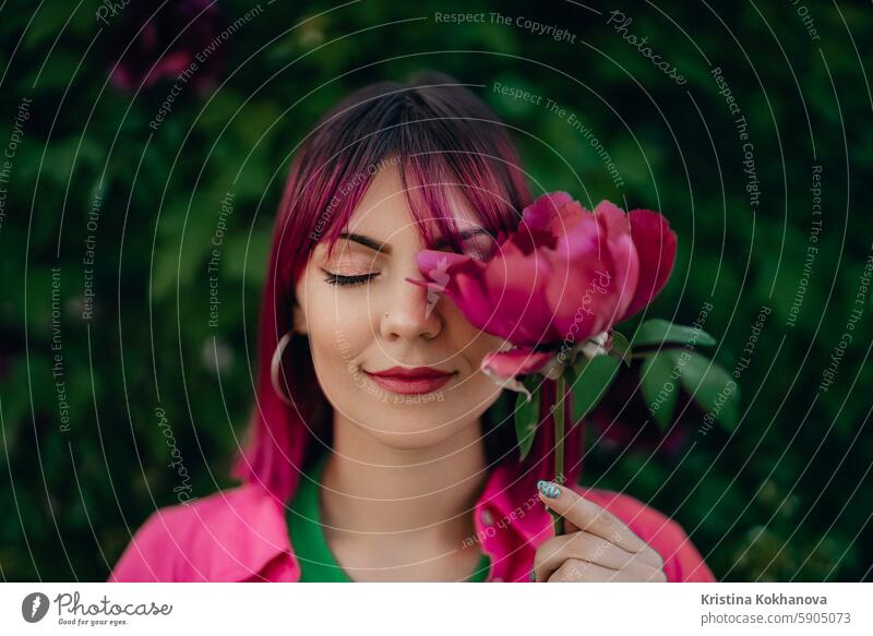 Porträt der realen heitere Frau mit lebendigen gefärbt rosa fuchsia Frisur. Pfingstrose Blume, grüner Natur-Hintergrund. Trendy bunte Haare, stilvolle Haarschnitt