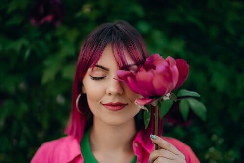 Porträt der realen heitere Frau mit lebendigen gefärbt rosa fuchsia Frisur. Pfingstrose Blume, grüner Natur-Hintergrund. Trendy bunte Haare, stilvolle Haarschnitt