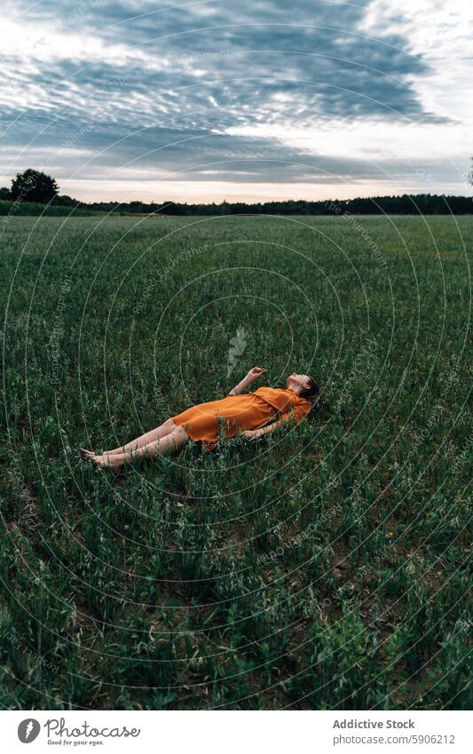 Frau entspannt sich auf einem Feld in orangefarbenem Kleid brünett Augen geschlossen orangefarbenes Kleid Natur Erholung Gelassenheit friedlich Ruhe grünes Gras