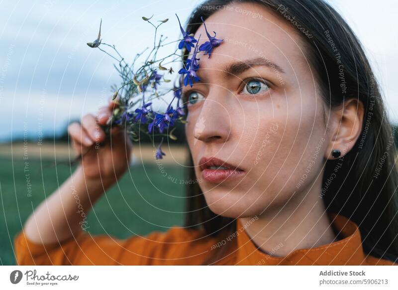 Brünette Frau hält Blumen auf einem Feld und schaut weg brünett Wegsehen Natur beschaulich Wildblumen Starrer Blick Anschluss im Freien Porträt nachdenklich