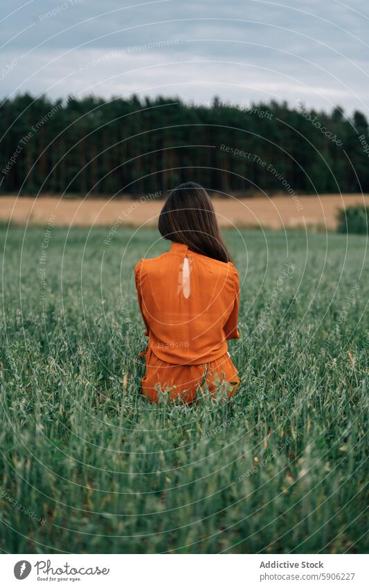 Brünette Frau in orangefarbenem Kleid steht auf einer grünen Wiese brünett Feld orangefarbenes Kleid allein Gelassenheit Natur im Freien pulsierend