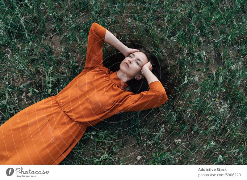 Junge brünette Frau entspannt sich auf einem Feld mit geschlossenen Augen Erholung Natur Gras Kleid orange Gelassenheit friedlich ruhen jung Wegsehen liegend