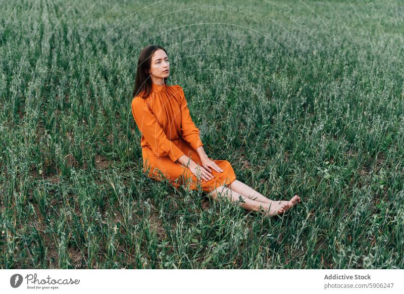 Frau entspannt sich auf einer grünen Wiese, gekleidet in Orange Feld orangefarbenes Kleid brünett nachdenklich beschaulich Natur im Freien Gelassenheit ruhig