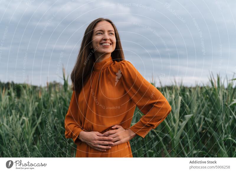 Brünette Frau lächelt auf einem Feld, schaut von der Kamera weg Gras brünett Kleid orange Lächeln Freude Fröhlichkeit im Freien Natur ländlich friedlich