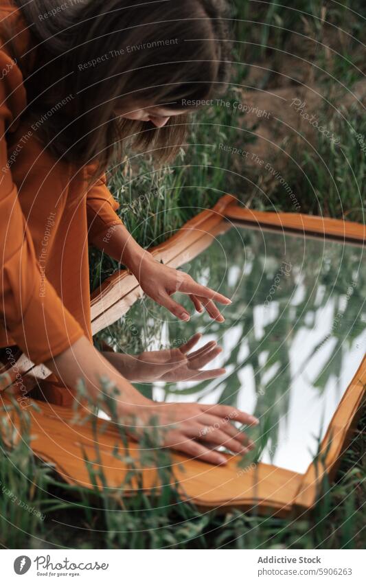 Brünette Frau interagiert mit Spiegel in grasbewachsenem Feld brünett Reflexion & Spiegelung Gras Kontemplation Erkundung im Freien Natur Gelassenheit Ruhe