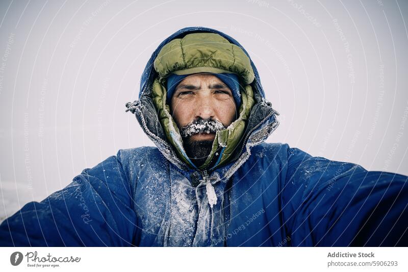 Männlicher Bergsteiger in gefrorener Ausrüstung trotzt dem strengen Winter männlich extrem kalt Kirgisistan Frost Vollbart Kapuze Starrer Blick