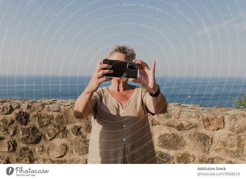Ältere Frau, die mit einem Smartphone eine schöne Aussicht festhält älter Handy Gerät Apparatur Fotografie malerisch Ansicht Küste MEER Landschaft im Freien