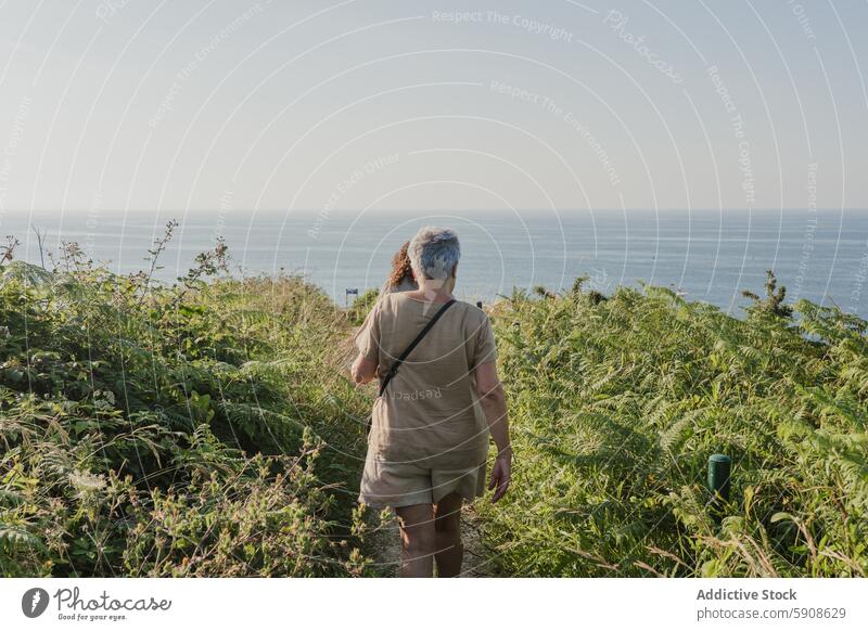 Ältere Frauen, die einen ruhigen Spaziergang am Meer genießen älter laufen Seeküste Natur Ruhe Klarer Himmel Küstenweg Grün im Freien Einsamkeit Erholung