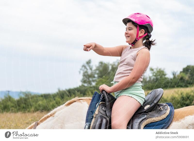 Junges Mädchen reitet auf einem Pferd und deutet in die Ferne Reiten Schutzhelm Zeigen Horizont Lächeln Sattel Reiterin Abenteuer im Freien ländlich Landschaft