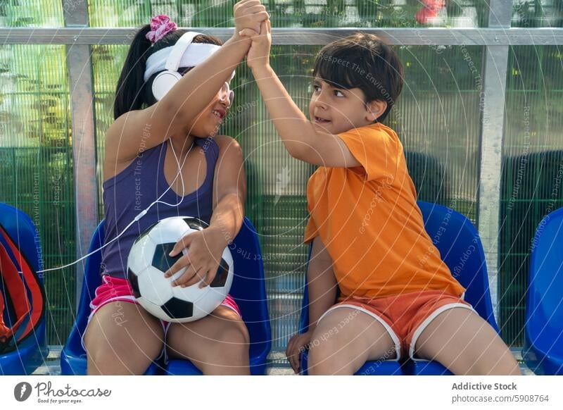 Zwei Kinder genießen einen spielerischen Moment mit einem Fußball Sport Ball Interaktion Freude spielen Feier high five Bank im Freien Zaun sitzen Sommer