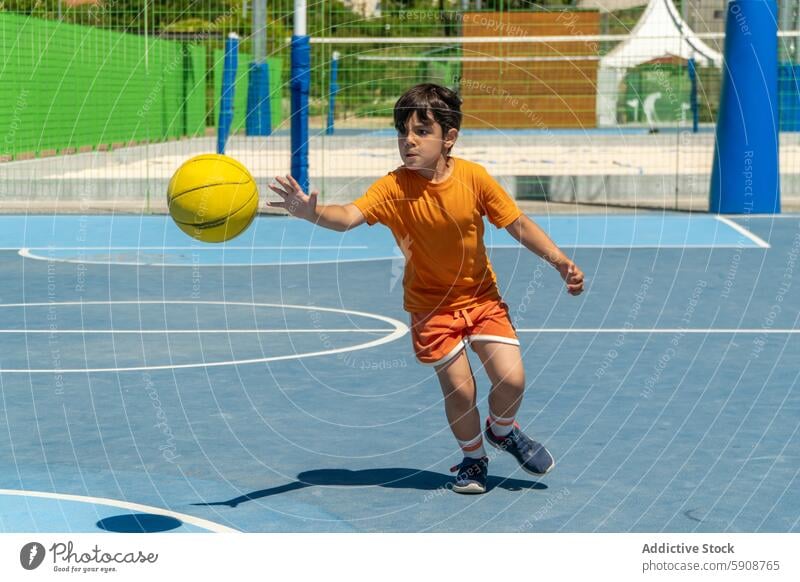 Junger Junge in Bewegung spielt Basketball im Freien Kind Sport Gericht Ball Spiel spielen Aktion aktiv Jugend Sportbekleidung sonnig Tageslicht physisch