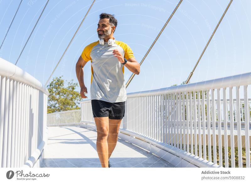 Indischer Mann joggt im Sommer mit Kopfhörern auf einer Brücke Inder Joggen Sportbekleidung Athlet rennen im Freien Fitness Übung aktiv Lifestyle Gesundheit